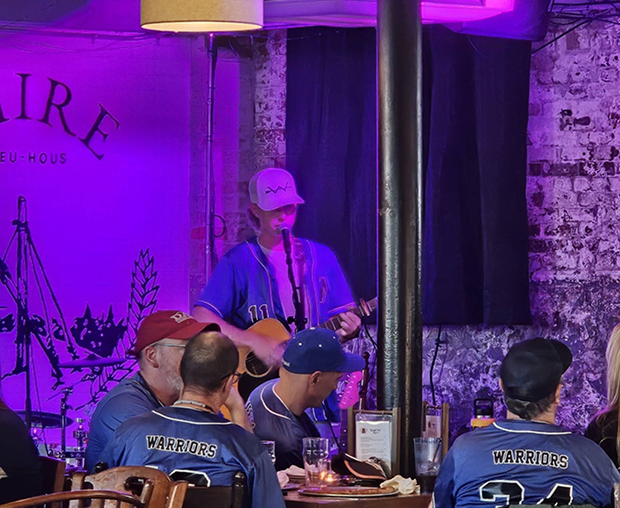 A musician performs live in a dimly lit venue with neon purple lighting.