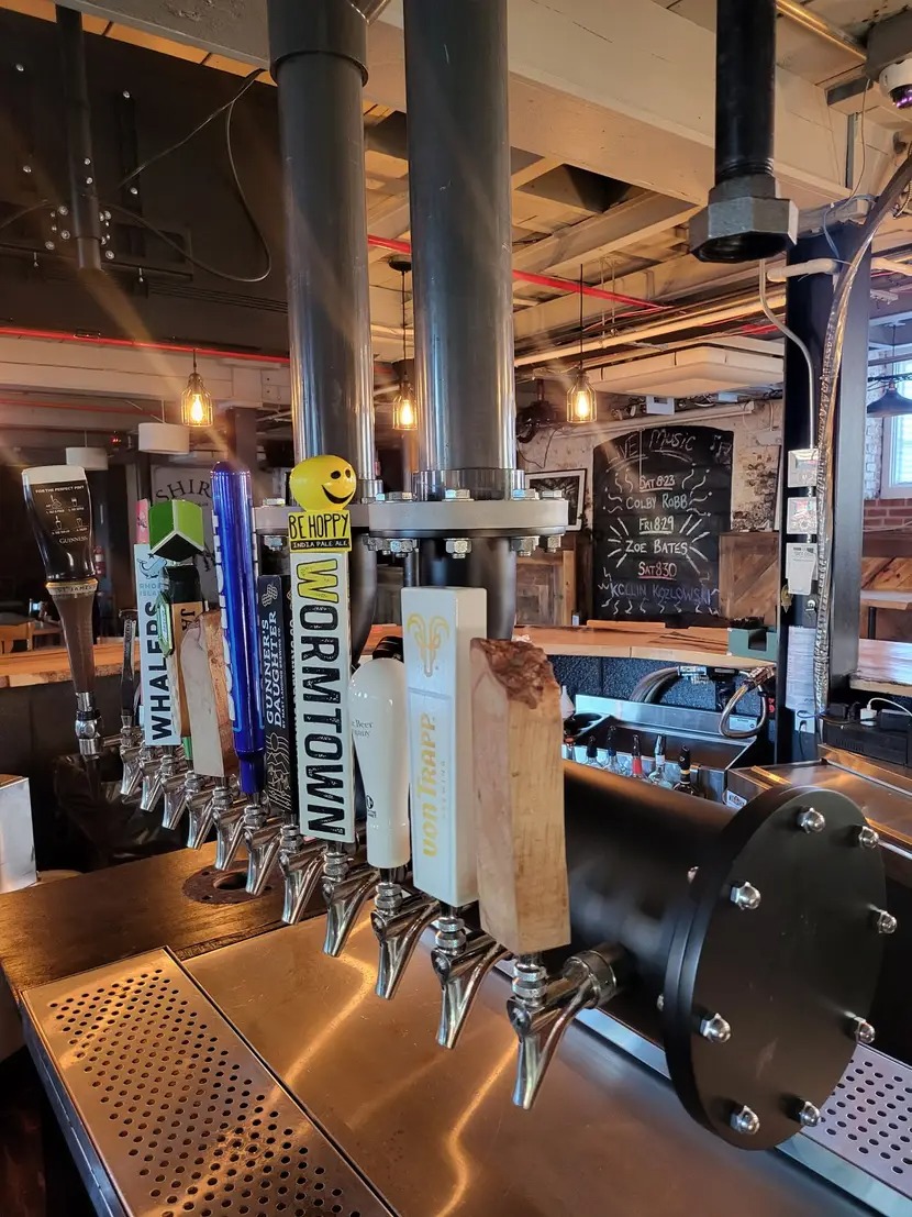 A row of diverse beer taps at a rustic bar counter.