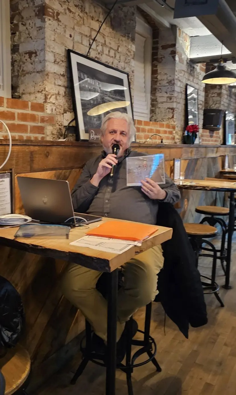 Man reading from paper while speaking into microphone at a rustic café.