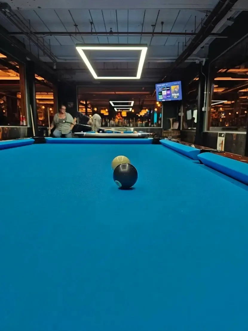 A close-up of a billiard cue ball on a blue pool table in a dimly lit room.